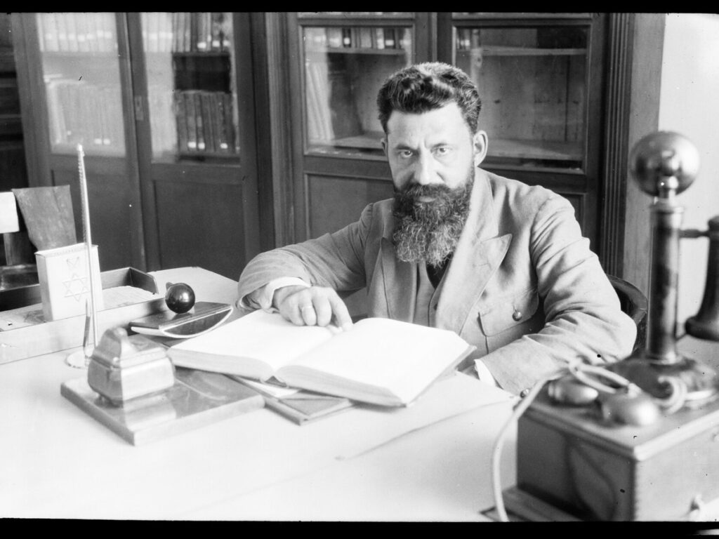 Man sitting behind a desk in an office. Open book in front of him, NINO F Scholten Tel Aviv 03 84