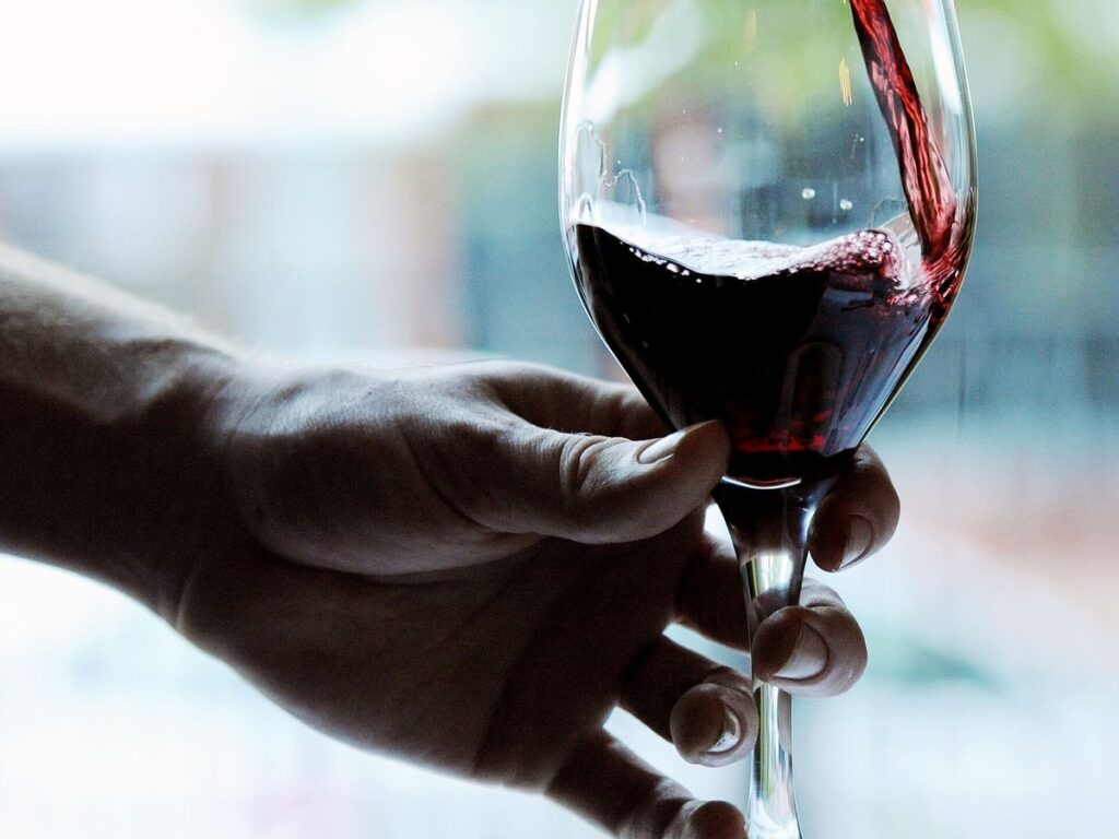 Close-up of red wine being poured into a glass with a blurred outdoor backdrop