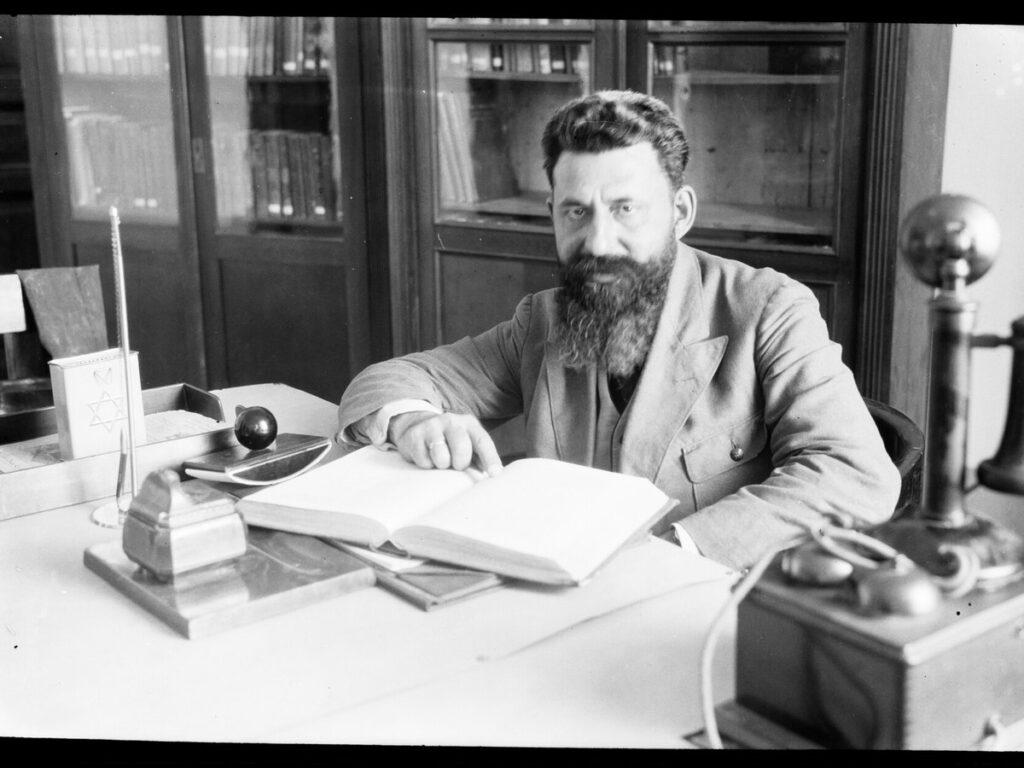 Man sitting behind a desk in an office. Open book in front of him, NINO F Scholten Tel Aviv 03 85